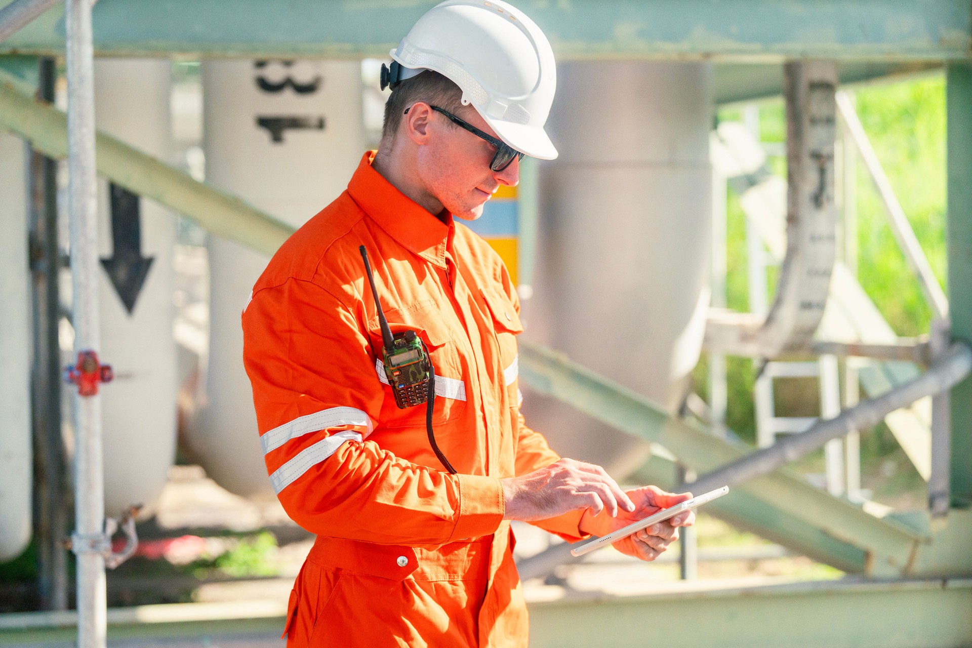 a man worker engineer conducts a site inspection at an industrial facility of gas and oil petroleum industry with utilizing a tablet for data management. technology and safety in maintaining operation